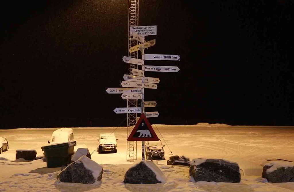 Signs pointing to different international destinations from Longyearbyen, Svalbard. A warning sign of a polar bear is found underneath.