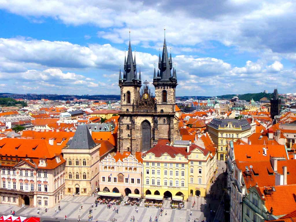 City skyline of Prague with a church and plaza in the foreground.